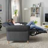 Woman relaxing in FAMMARP recliner, adjustable sofa, books, lamp, big window.