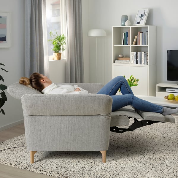 Woman relaxing on a reclining armchair, feet elevated, in a cozy living room with books, plants, and a tv.