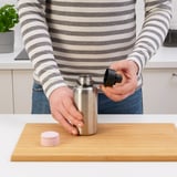 Person placing a black lid on a silver sports bottle on a cutting board.