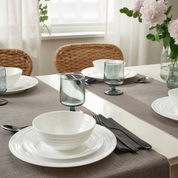 FAVORISERA dinnerware set on gray tablecloth, vase of pink flowers.