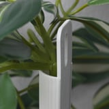 White wall-mounted planter holds green artificial plant; realistic leaves and sturdy support.