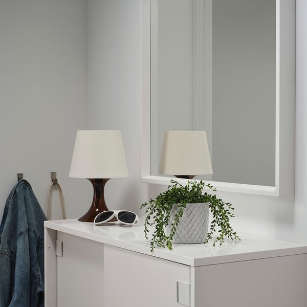 Small white FEJKA potted plant between two lamps on a narrow cabinet, near a blue denim jacket.