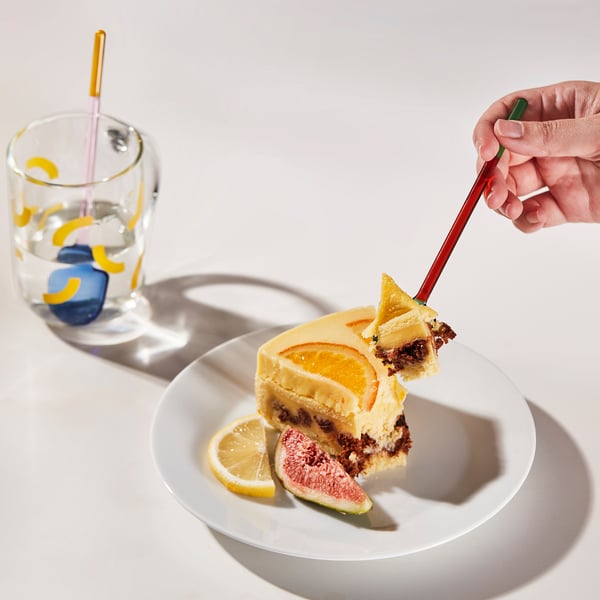 Hand holding colorful spoon serving cake with fruit.