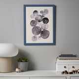 Modern art print in blue frame above white table with lamp, plant, and books.