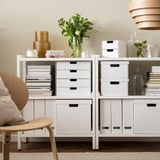 White FJÄDERHARV boxes on shelves, holding books, flowers, and decor. Ideal for workspace and living room, blending functionality and modern design.