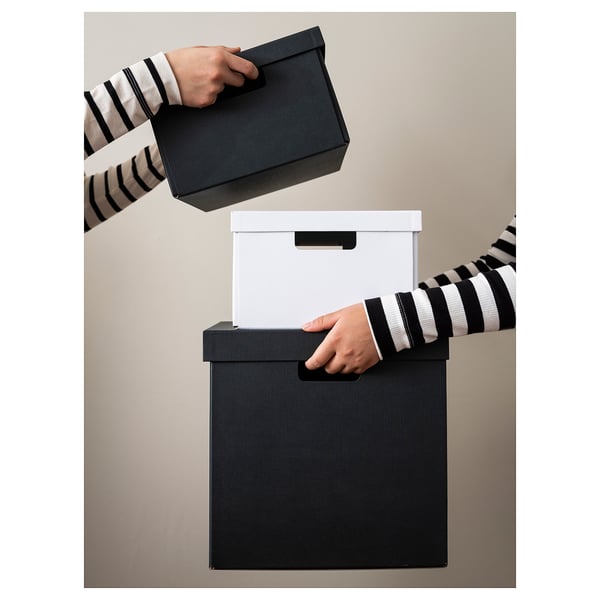 A person holding black and white storage boxes. The black box has a handle, and a white box with a lid is visible in the background.