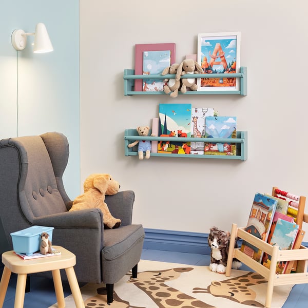 Cozy kids reading nook with wall shelves holding books and stuffed toys, grey armchair, and wooden stool.