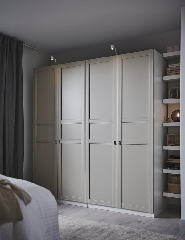 Bedroom with tall FLISBERGET wardrobe, light gray, three-panel doors, soft-closing hinges, wooden floor, and decoration shelves.