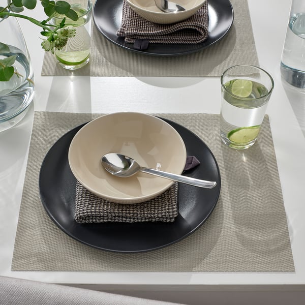 Table setting with beige bowls, spoons, black plates, gray mats, and water with lime.