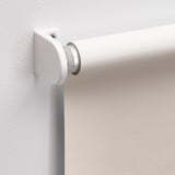 White roller blind bracket mounted on wall, holding smooth, light-blocking blind.