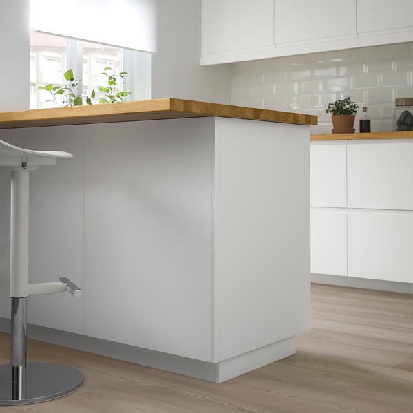 A modern white kitchen island with a wooden top and cabinets. A potted plant adds greenery.
