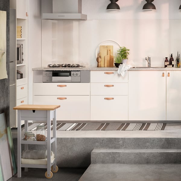 Modern kitchen with white FÖRHÖJA trolley, birch drawers, copper handles, grey countertop, wheels, pendant lights.