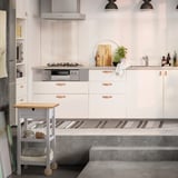 Modern kitchen with white FÖRHÖJA trolley, birch drawers, copper handles, grey countertop, wheels, pendant lights.