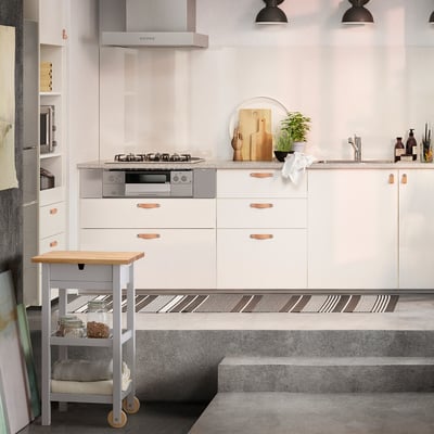 Modern kitchen with white FÖRHÖJA trolley, birch drawers, copper handles, grey countertop, wheels, pendant lights.