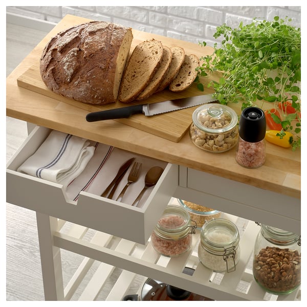 A wooden kitchen trolley with drawers and cabinets, displaying bread, cutlery, and food items.