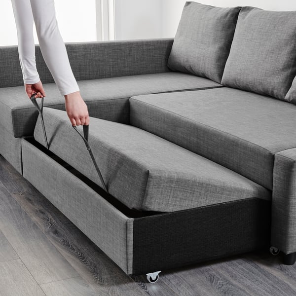 Image depicts a person converting a grey corner sofa into a bed by pulling out the chaise longue section, revealing storage underneath.
