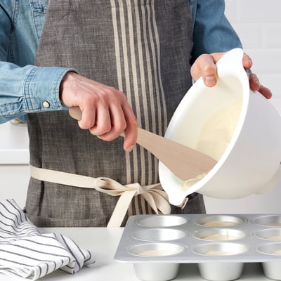 Person pouring batter from a bowl into a muffin tin.