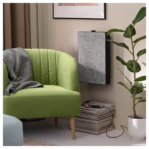 A cozy green barrel chair with wooden legs next to a speaker and a plant.