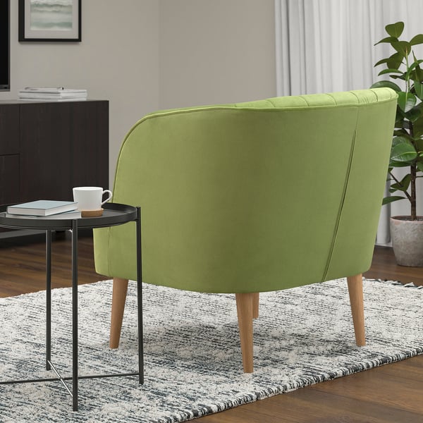 Green barrel chair with wooden legs on a patterned rug, beside a metal side table with a cup and coaster.