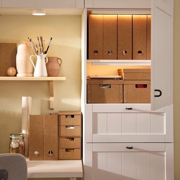 White storage units with brown cardboard inserts, storing art supplies. Varying sizes, labeled, maximize space.