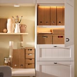 White storage units with brown cardboard inserts, storing art supplies. Varying sizes, labeled, maximize space.