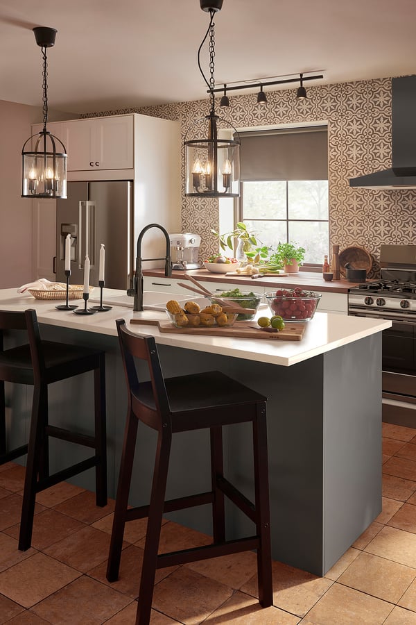 Modern kitchen with white cabinets, black stools, and GALJON pendant lamps. Patterned backsplash, fresh produce, and plants on island.