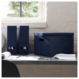 Blue GJÄTTA storage boxes on desk. Two vertical file holders, one box. Paperboard & polyester, sleek design.