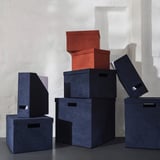 Stacks of GJÄTTA magazine holders, including velvet-covered dark blue and red boxes. Larger boxes hold smaller ones, showcasing varying sizes.