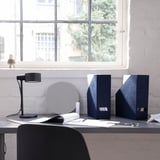Blue velvet GJÄTTA magazine holder, desk lamp, mirror, and supplies by a window.