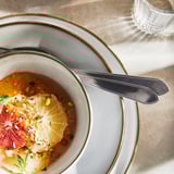 Sandy-colored glazed ceramic bowl with fruit, knife, and spoon. Elegant, rustic design.