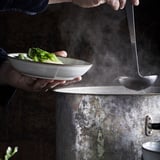 Hands holding glazed bowl with green veggies over steamer.