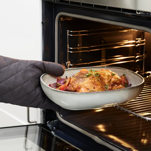 Person places roasted chicken, veggies in oven dish.