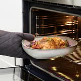 Person places roasted chicken, veggies in oven dish.