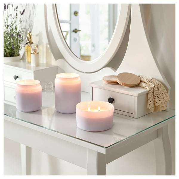 Three lit lavender candles in glass jars on a glass table with a mirror and box, creating a calm ambiance.