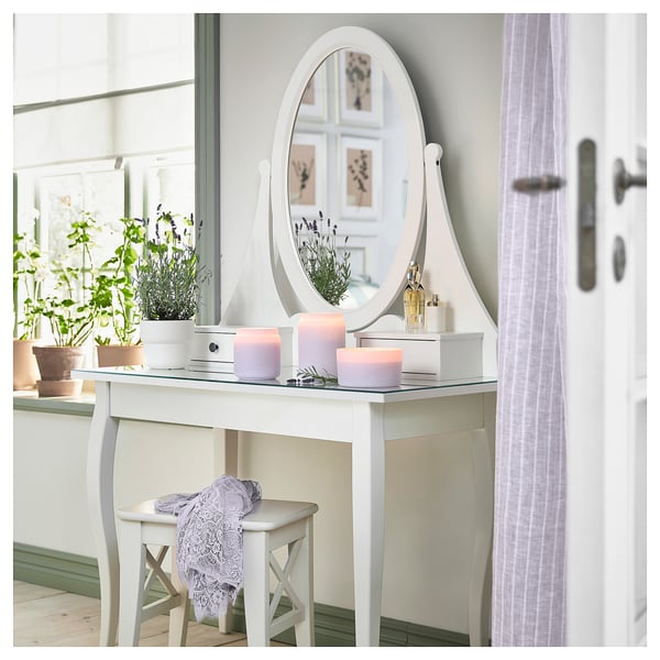 White vanity with mirror, purple candles, flowers, and a plant.