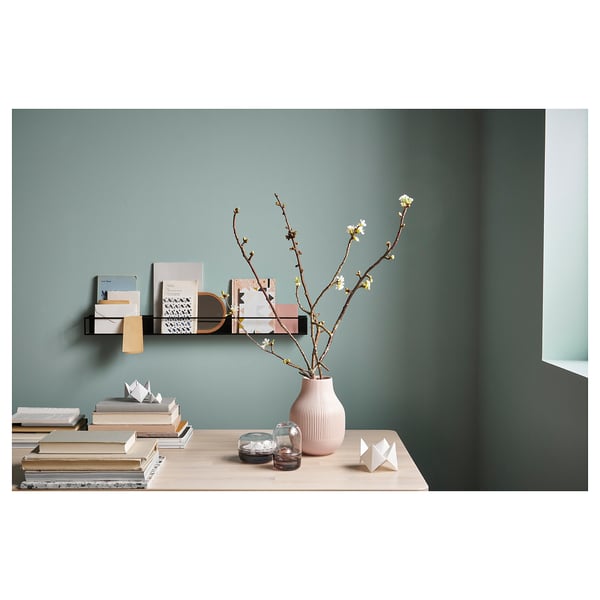Modern living space with wood table, books, candles, and vase with flowers. Black and white shelf above with books and decor.