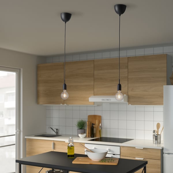 Small black pendant lights hang from the ceiling, illuminating a kitchen island with wooden cabinets and white tiles.