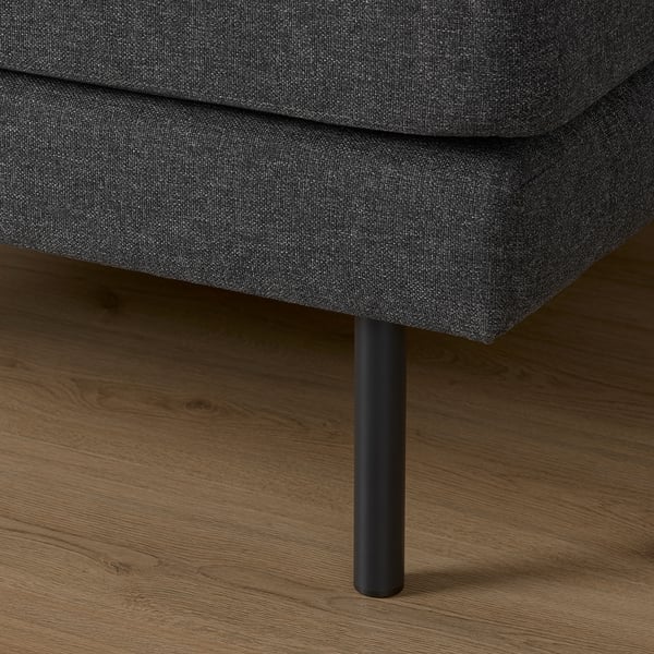 Dark gray upholstered sofa corner with sleek black metal leg on wooden floor.
