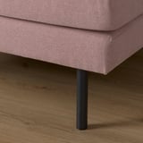 Close-up of a pink fabric sofa with black metal legs on light wooden floor.