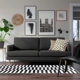 Modern living room with GRILLSTORP gray sofa; cushioned, cool art wall, black/white rug.