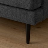 Close-up of dark grey GRILLSTORP sofa on hardwood floor, showcasing sleek leg design and durable fabric.