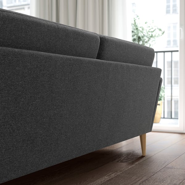 A modern charcoal 4-seat sofa with wooden legs positioned near a large window, showcasing its sleek, inviting design.