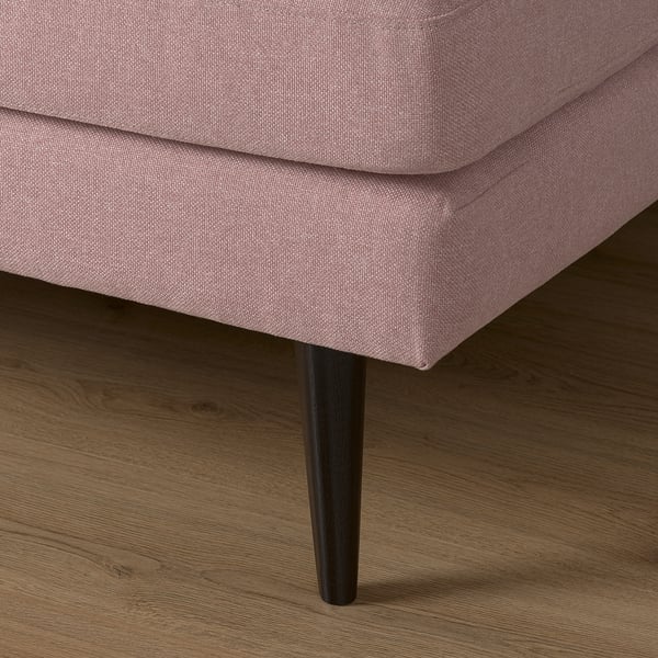 Pink fabric sofa with black tapered legs on a wooden floor.
