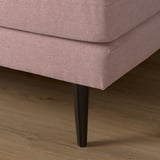 Pink fabric sofa with black tapered legs on a wooden floor.
