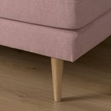 Close-up of a pink sofa with wooden legs on a wooden floor.