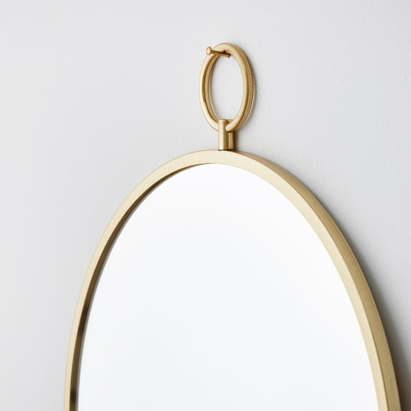 Gold-framed round mirror hangs securely on wall. Clear, reflective surface, elegant brass details.