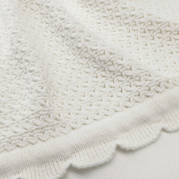 Close-up soft white knitted blanket, textured, intricate stitch design.