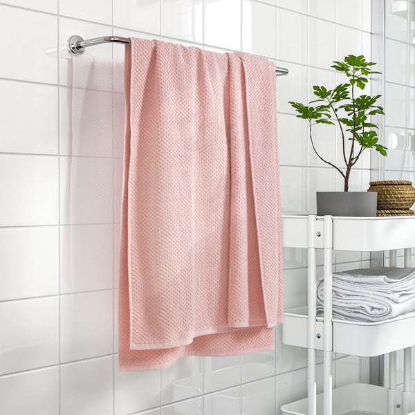 Scroll towel bar with light pink, textured GULVIAL towel beside white storage unit and plant.