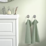 Modern bathroom with white vanity, chrome, 2 green towels, & small decor.