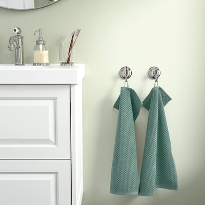 Teal towels hang on chrome hooks by white vanity on green wall.